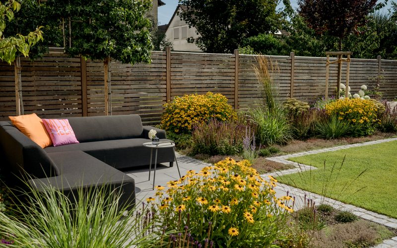 Terrasse mit Lounge-Möbeln, umgeben von Gräsern und blühenden Stauden