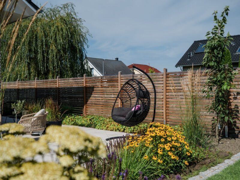 Terrasse mit Hängesessel, davor ein Beet aus Gräsern und Sommerstauden