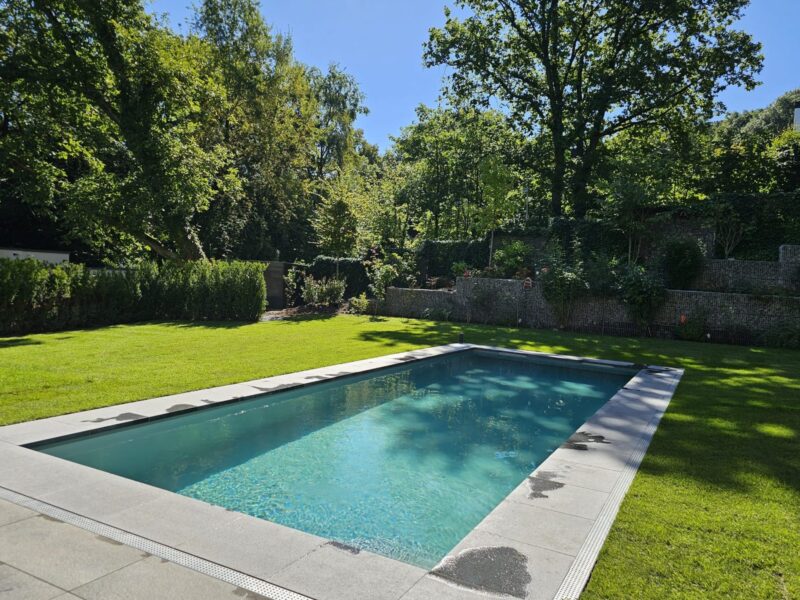 Schwimmbecken mit Natursteinmauer und Rasenfläche im parkartigen Garten